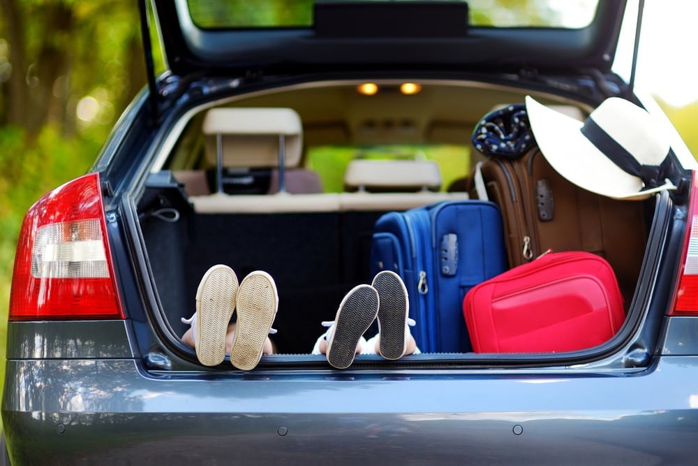 Little kids put their feet up in the back of a car filled with suitcases.