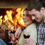 Romantic couple drinking wine next to the fireplace.