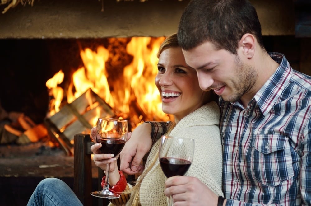 Romantic couple drinking wine next to the fireplace.