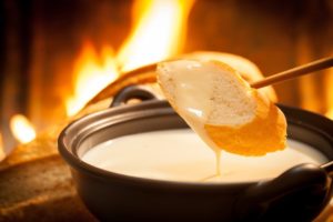 A piece of bread being dipped in cheese fondue.